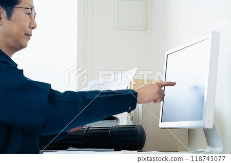 A man in work clothes comparing a computer and documents A man in work clothes comparing a computer and documents 118745077