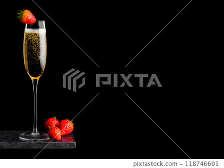 Elegant glass of yellow champagne with strawberry on top and fresh berries on black marble board on black background. Space for text Elegant glass of yellow champagne with strawberry on top and fresh berries on black marble board on black background. Space for text 118746691