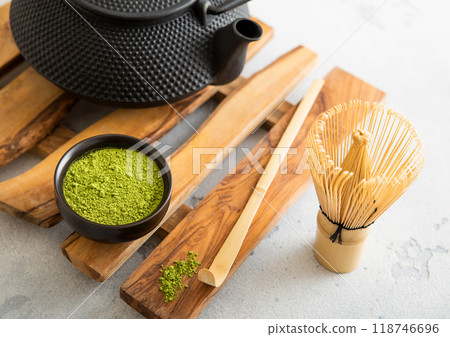 Matcha green organic tea powder with iron cast kettle with bamboo whisk and spoon on wooden tray on white. 118746696