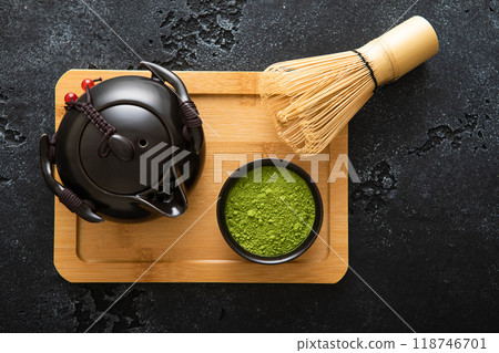 Green matcha tea powder with bamboo whisk and ceramic kettle on wooden board on black background.Top view. Green matcha tea powder with bamboo whisk and ceramic kettle on wooden board on black background.Top view. 118746701