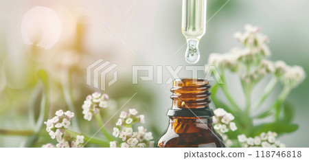 Close-up of a dropper placing essential oils into an amber bottle, with delicate white flowers in the background, suggesting natural aromatherapy. 118746818