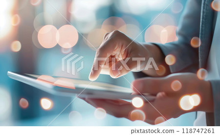 Close-up of a person's hand using a tablet with a bokeh background. Concept of modern technology and connectivity. Close-up of a person's hand using a tablet with a bokeh background. Concept of modern technology and connectivity. 118747261