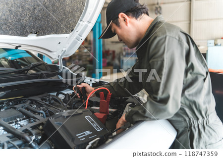 Male mechanic using a battery jump starter 118747359