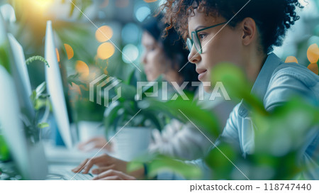 Focused professionals working on computers in a modern office with indoor plants, highlighting concentration and productivity. 118747440