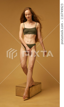Full-length portrait of tender young woman with slim, beautiful body shape, posing in underwear against sandy color studio background 118749923