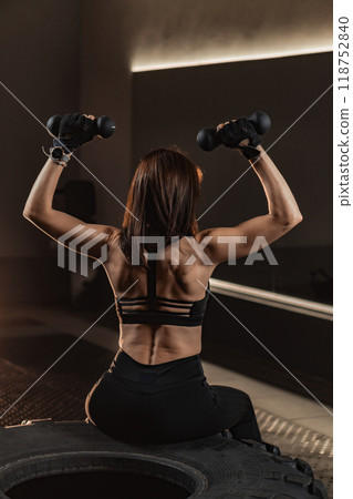 In a modern gym, a strong woman lifts dumbbells, showcasing her commitment to health and fitness, inspiring others to start their wellness journeys and fostering a community focused on strength 118752840