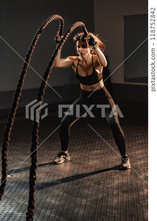 Engaging in a Dynamic Workout with Battle Ropes set in a Contemporary Gym Environment for an energized fitness experience. Ideal for those dedicating themselves to achieving optimal health 118752842