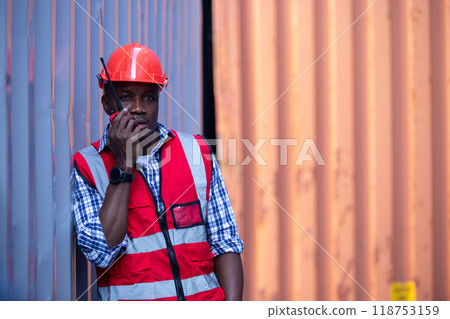 Man american african with talkie walkie at worker industry dock or container yard. foreman talking radio working control forklift loading cargo shipping transport. 118753159