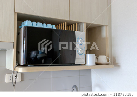 black-and-white microwave placed on a wooden kitchen shelf.  118753193