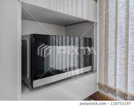 black-and-white microwave placed on a wooden kitchen shelf. 118753197