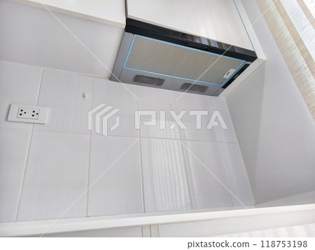 Modern kitchen design featuring a sleek electric stovetop with a black glass surface and a built-in exhaust hood. Minimalist and clean, perfect for small spaces and contemporary interiors. 118753198