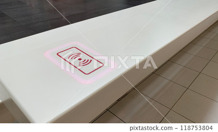 Tabletop with sticker indicating place for wireless charging of phone, modern electricity technologies for charging device without wire, put down phone on surface and charge battery Tabletop with sticker indicating place for wireless charging of phone, modern electricity technologies for charging device without wire, put down phone on surface and charge battery 118753804