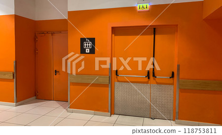 Corridor of building with orange walls next to door to elevator, a sign with admission of four people to occupancy of elevator and sign for disabled person for special elevator Corridor of building with orange walls next to door to elevator, a sign with admission of four people to occupancy of elevator and sign for disabled person for special elevator 118753811