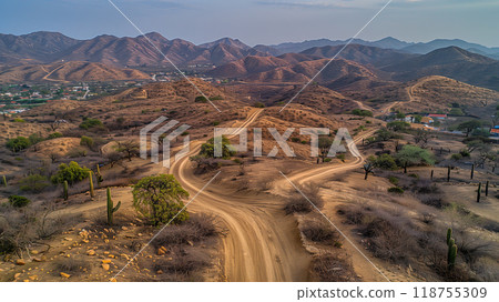 Scenic Dirt Road Winding Through Hilly Terrain in a Desert Landscape During Late Afternoon Scenic Dirt Road Winding Through Hilly Terrain in a Desert Landscape During Late Afternoon 118755309