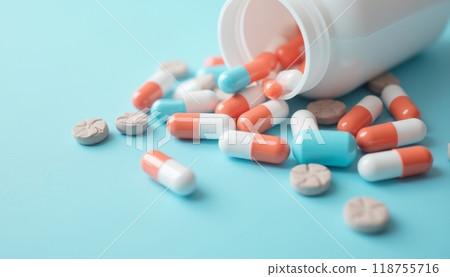 A bottle of assorted pills spills onto a light blue surface, symbolizing healthcare, medicine, and pharmaceutical industry. 118755716