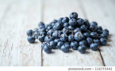 A pile of fresh blueberries sits on a rustic wooden table, showcasing the vibrant blue color and natural texture of the fruit. The scene evokes freshness and healthy eating. 118755842