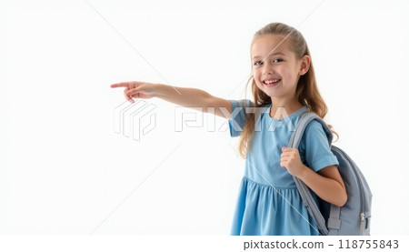 A cheerful young girl in a blue dress and backpack smiles and points with excitement, symbolizing school, learning, or a new adventure. The white background highlights her joy. 118755843