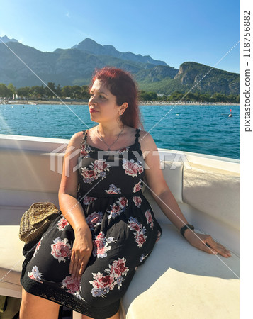 Woman in a black dress sits on a boat under the bright sun, with a scenic view of mountains and the sea in the background. Moment of tranquility and natural beauty concept. Vacation, travel and voyage Woman in a black dress sits on a boat under the bright sun, with a scenic view of mountains and the sea in the background. Moment of tranquility and natural beauty concept. Vacation, travel and voyage 118756882