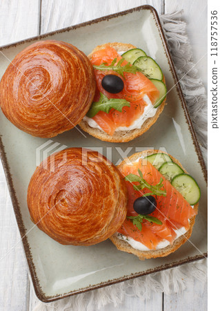 Crescent roll sandwich with salmon, cream cheese, fresh cucumbers and olives close-up on a plate. Vertical top view 118757536
