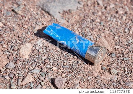 Plastic sleeve for a hunting-type cartridge for a smoothbore shotgun. Empty blue gun casing on a dirt road. Plastic sleeve for a hunting-type cartridge for a smoothbore shotgun. Empty blue gun casing on a dirt road. 118757878