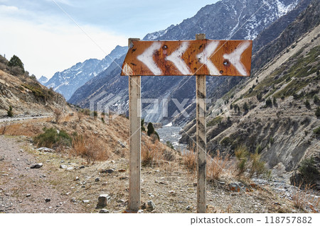 Red road sign with white left turn arrows on the roadside in the mountains 118757882