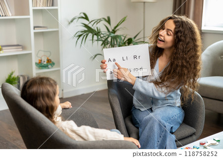 Curly-haired speech therapist demonstrating tables with syllabled to a kid 118758252