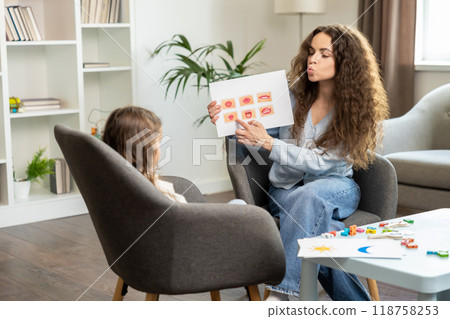 Curly-haired speech therapist demonstrating tables with syllabled to a kid Curly-haired speech therapist demonstrating tables with syllabled to a kid 118758253