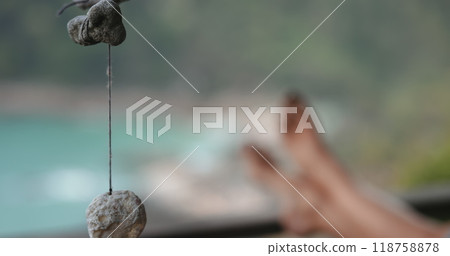 Relax and quiet outdoor concept. Shells and corals on threads swaying in the wind. Barefoot legs in background, close up seashells strung on a rope sway by the sea. Slow Relax and quiet outdoor concept. Shells and corals on threads swaying in the wind. Barefoot legs in background, close up seashells strung on a rope sway by the sea. Slow 118758878