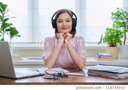 Portrait of young female student wearing headphones, sitting at home at desk 118759142