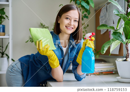 Portrait of young woman cleaning house, wearing gloves with cleaning spray looking at camera Portrait of young woman cleaning house, wearing gloves with cleaning spray looking at camera 118759153