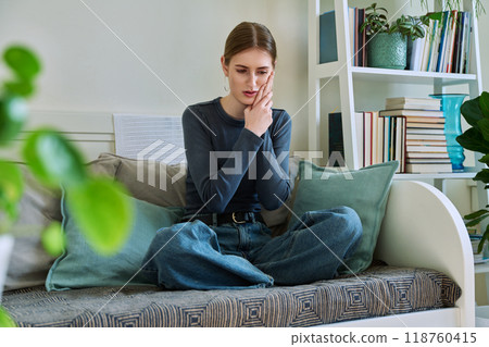 Young teenage female having toothache, sitting on couch at home Young teenage female having toothache, sitting on couch at home 118760415