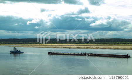 A large river vessel pulls two barges loaded with timber down the river A large river vessel pulls two barges loaded with timber down the river 118760601