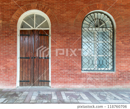 A rustic wooden door and iron-barred window on a historic red brick building in a tranquil setting A rustic wooden door and iron-barred window on a historic red brick building in a tranquil setting 118760706