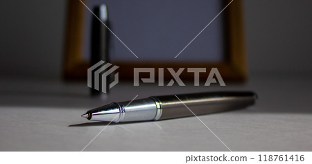 Pen on beautiful white fon on warm light. Wooden picture frame and cap in the background. 118761416
