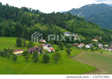 Lush green hills frame quaint village houses nestled in the valley under overcast skies during a tranquil summer afternoon Lush green hills frame quaint village houses nestled in the valley under overcast skies during a tranquil summer afternoon 118761460