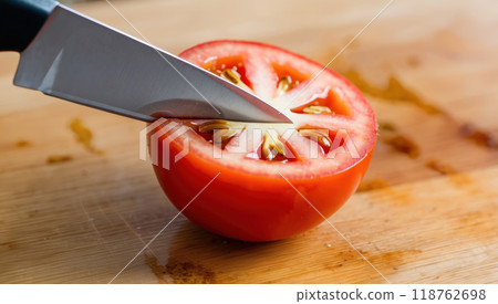 knife slicing a ripe tomato on a wooden board, showcasing freshness 118762698