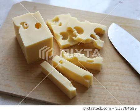 Cheese with holes cut into pieces lies next to a knife on a wooden board on a white background. Cheese making and dairy products. Kitchen, cooking, appetite. Dutch maasdam cheese Cheese with holes cut into pieces lies next to a knife on a wooden board on a white background. Cheese making and dairy products. Kitchen, cooking, appetite. Dutch maasdam cheese 118764689