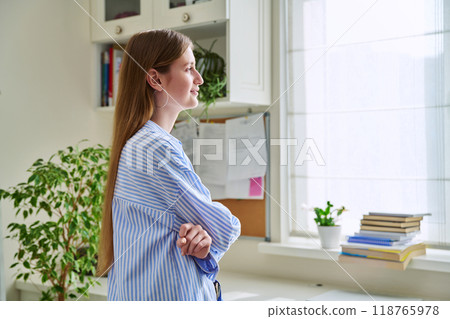 Smiling young woman looking out the window, in home interior 118765978