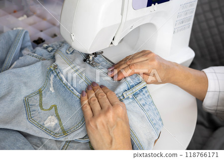 Clothes repair concept. Women's close-up hands sew up old faded blue jeans. 118766171
