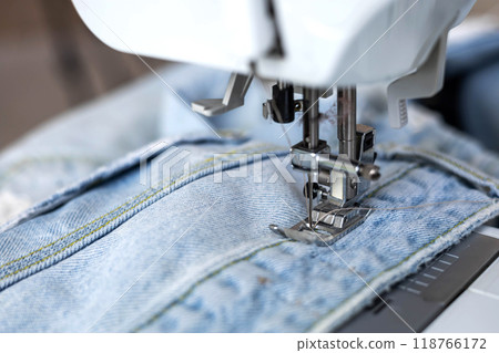 Close-up of a sewing machine foot making a stitch on blue jeans. 118766172