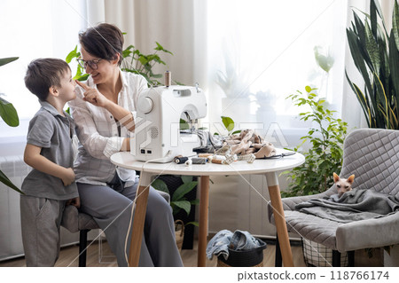 Mom are at home repairing old torn jeans using a sewing machine. A woman teaches a son to sew. Mom are at home repairing old torn jeans using a sewing machine. A woman teaches a son to sew. 118766174