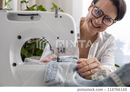 A woman at home repairs old torn jeans on a sewing machine. A woman at home repairs old torn jeans on a sewing machine. 118766188