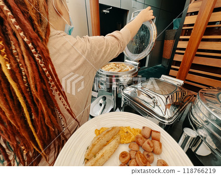 In a first-person perspective, a man is meticulously plating a dish. In a hotel, a woman is choosing food from a warming machine to fill up her plate at the buffet. 118766219