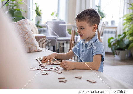 A Caucasian light-haired boy of five years old with blue eyes is putting together a puzzle 118766961