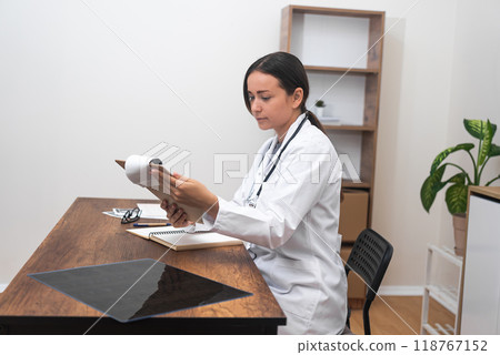 Therapist's Dedication: A young female therapist doctor, working in a modern clinic, dedicates herself to the meticulous examination of patient test results. Therapist's Dedication: A young female therapist doctor, working in a modern clinic, dedicates herself to the meticulous examination of patient test results. 118767152
