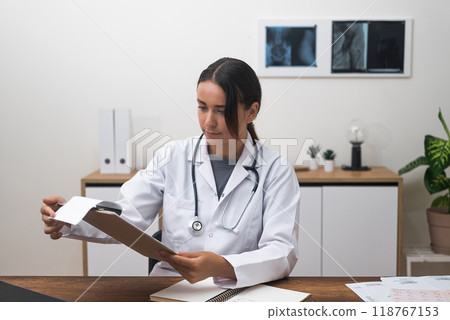 Medical portrait: A female doctor in uniform assesses patient test findings at her clinic desk, underscoring modern healthcare innovations. Medical portrait: A female doctor in uniform assesses patient test findings at her clinic desk, underscoring modern healthcare innovations. 118767153
