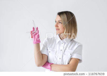 A female gynecologist doctor in a medical uniform and pink gloves on a white studio background with a plastic Speculum in hands 118767639