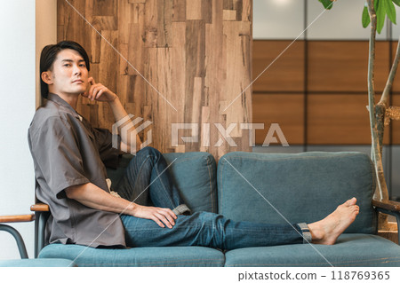 一個年輕的亞洲男子在沙發上度過無聊的時光(無聊、無聊、沮喪、昏昏欲睡、遲鈍、疲倦、憤怒) 一個年輕的亞洲男子在沙發上度過無聊的時光(無聊、無聊、沮喪、昏昏欲睡、遲鈍、疲倦、憤怒) 118769365