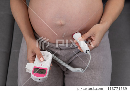 Close-up of a pregnant woman's belly using a home doppler. Normal baby heartbeat. 118771589