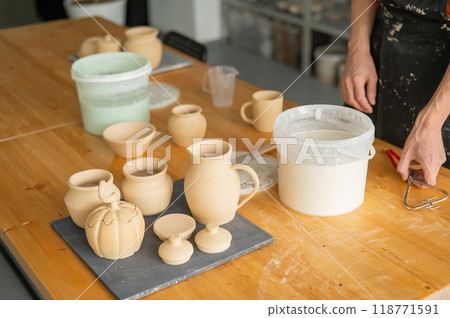 Close-up of a potter's hands glazing a ceramic mug.  118771591